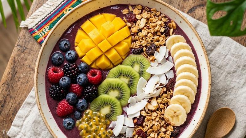 A thick purple acai smoothie bowl topped with sliced banana, granola, coconut flakes, and fresh berries